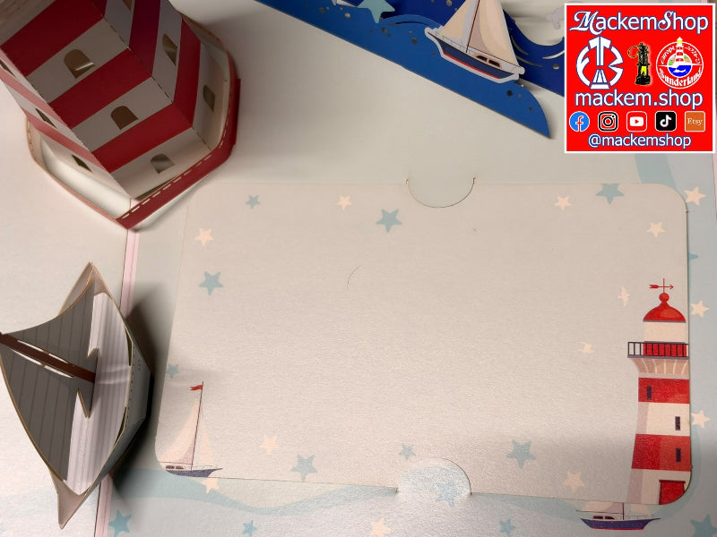 A nautical-themed paper craft card set featuring a central white card with blue stars, a red-and-white striped lighthouse, a paper boat, and a blue sailboat on a white background. A 'MackemShop' logo overlay is visible in the top right corner.