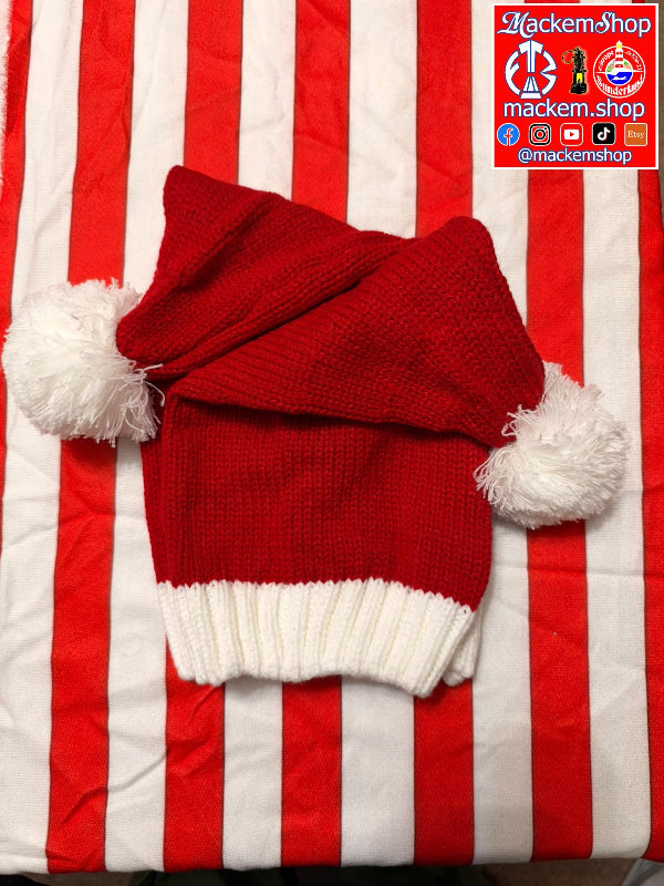 A red knit Santa hat with white pom-poms and a white ribbed cuff, laid flat on a red and white striped fabric background. A 'MackemShop' logo watermark is visible in the top right corner.