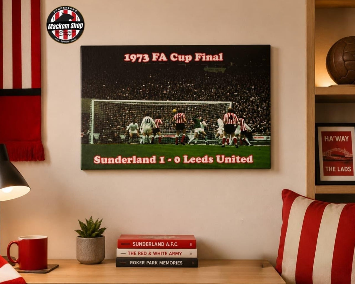 A framed 1973 FA Cup Final poster featuring Sunderland 1 - 0 Leeds United, displayed on a wall in a cozy room setting with a red and white striped pillow, a mug, and books on a wooden table.