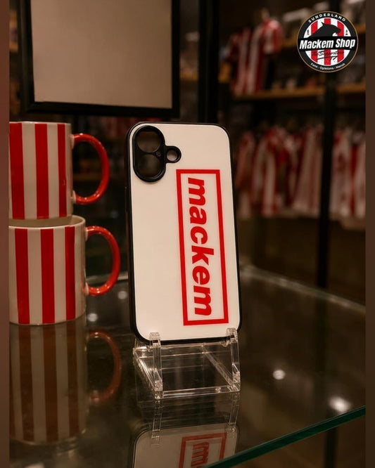 A white phone case with a red 'mackem' logo displayed on a clear stand on a glass shelf, with red and white striped mugs in the background.