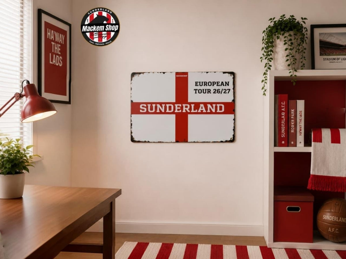 A rectangular vintage-style Sunderland football club sign with a red St George's cross on a distressed white background, hanging on a beige wall in a styled room with a desk, lamp, shelf, and plants.