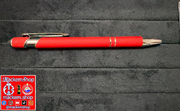 A red and silver ballpoint pen resting on a dark gray textured fabric surface, with a MackemShop logo overlay in the bottom-left corner.