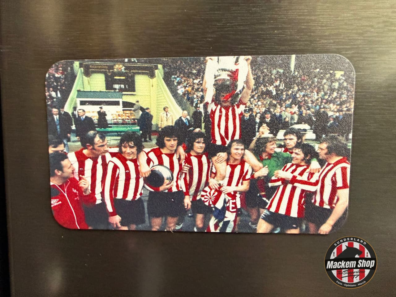 Fridge magnet with a soccer team celebrating on a metallic surface, featuring the Macken Shop logo.