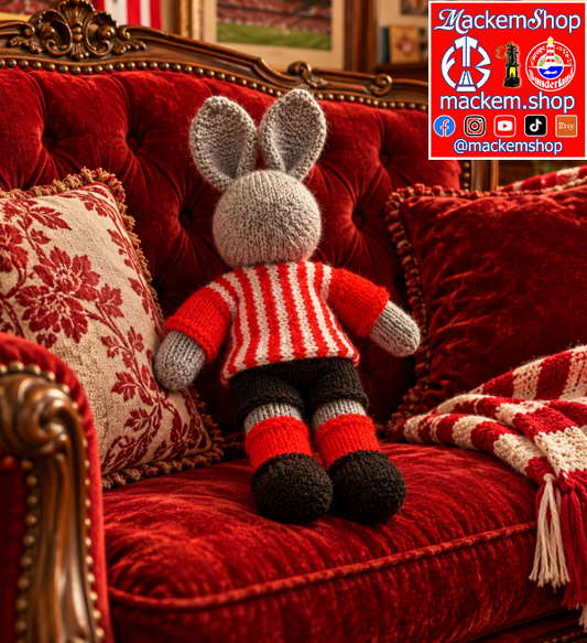 A red and white hand knitted Rabbit is laying on a sofa, with A MackemShop Logo is visible on top right corner.