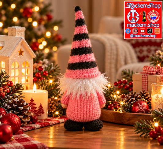 Pink and black knitted Christmas gonk, featuring a striped pointed hat, fluffy white beard, pink body and black feet, displayed on a wooden table with festive Christmas decorations, pinecones, red ornaments, candles and warm fairy lights.
A MackemShop Logo is Visible on top right corner.