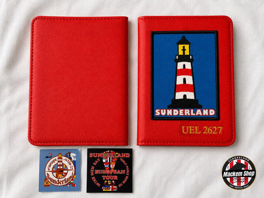 A red faux-leather passport cover shown closed and open, with a printed Sunderland lighthouse patch on the inside cover. Two small printed inserts are placed below, and a circular 'Macken Shop' logo appears in the lower right corner, all laid on a white fabric background.