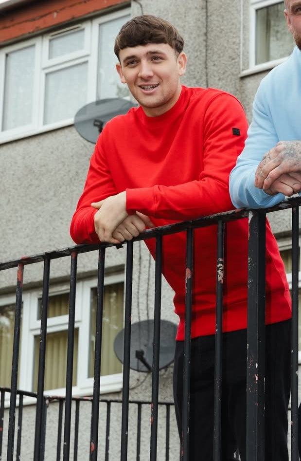 Two people standing on a balcony with one wearing a Terrace Cult Red Sweatshirt by Mackem Shop.