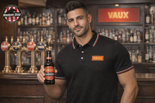 Man holding a Vaux beer bottle while wearing a VAUX polo shirt in a bar setting