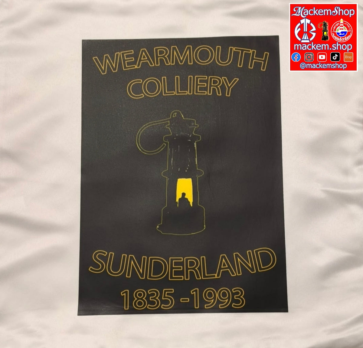 A Cushion pillowcase with gold/yellow text reading 'WEARMOUTH COLLIERY' at the top, a lantern illustration in the center, and 'SUNDERLAND 1835-1993' at the bottom, placed on a white fabric background. A 'Mackem-Shop' logo appears in the top-right corner.