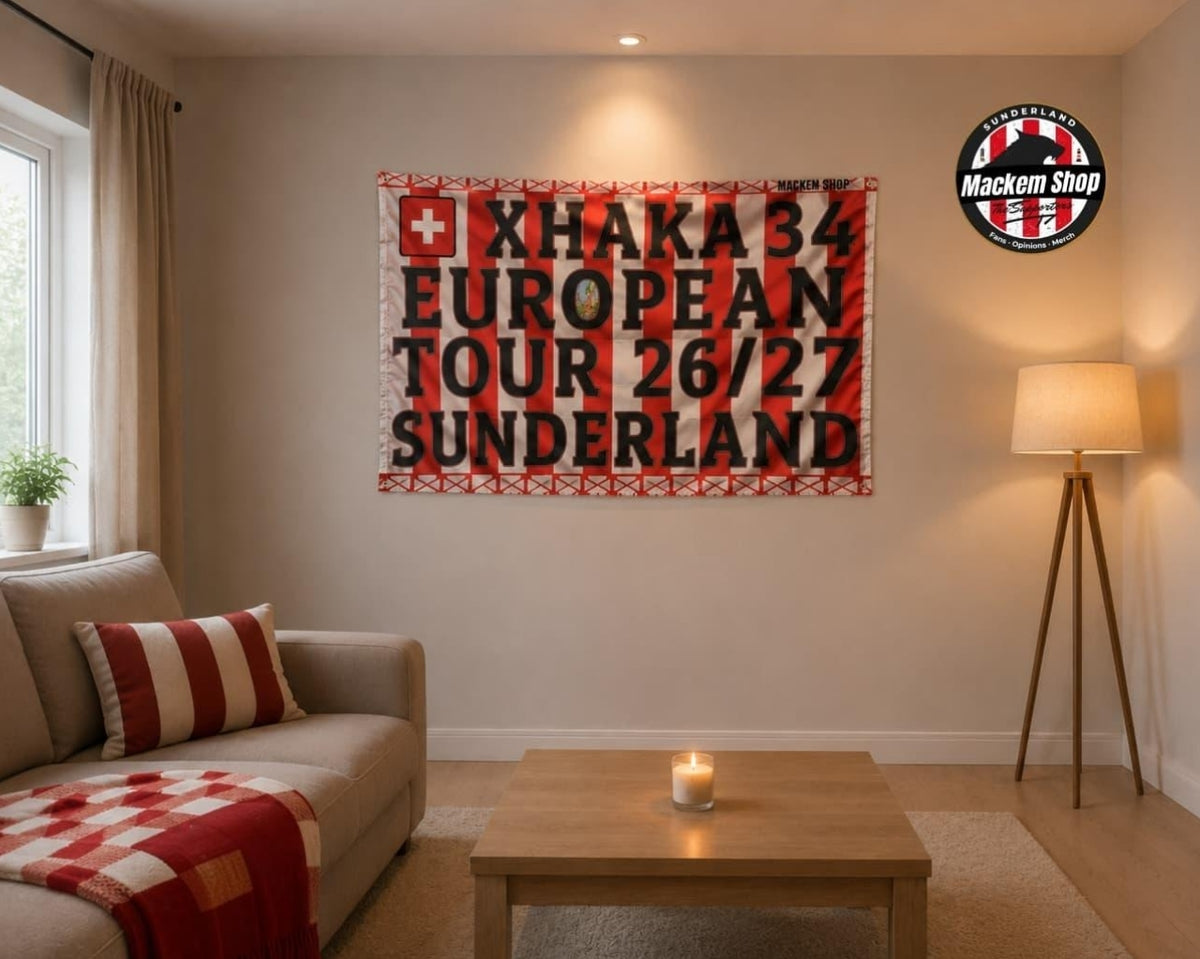 A red and white striped Flag celebrating 'XHAKA 34 EUROPEAN TOUR 26/27 SUNDERLAND' is displayed on a beige wall in a cozy living room setting with a sofa, coffee table, and floor lamp.