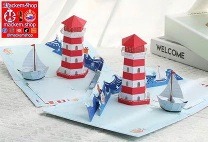 A 3D pop-up paper card featuring a nautical theme with two red and white striped lighthouses, blue waves, and small paper boats, displayed on a light textured surface, with MackemShop Logo visible on top left corner.