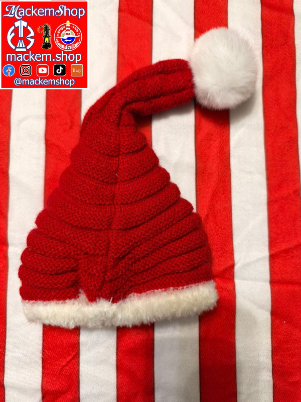A red knitted Santa hat with a white faux-fur trim and pom-pom, laid flat on a red and white striped fabric background. A red brand watermark for MackemShop is visible in the top-left corner.