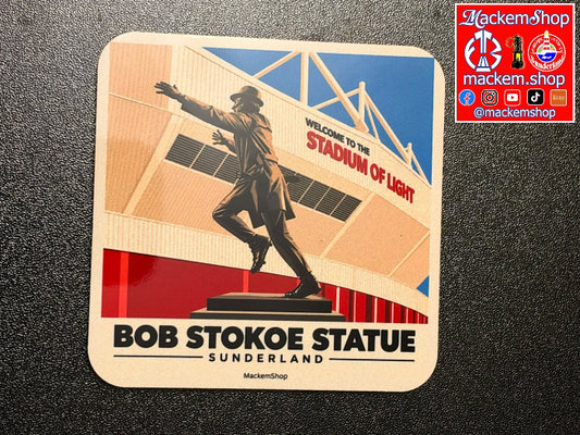 A square printed coaster featuring a stylized illustration of the Bob Stokoe Statue at Sunderland, with stadium architecture and the text 'Welcome to the Stadium of Light' and 'Bob Stokoe Statue Sunderland.' A MackemShop logo appears in the top-right corner of the image, and the coaster itself is photographed on a dark textured surface.