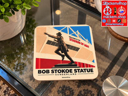 A square printed coaster featuring a stylized illustration of the Bob Stokoe Statue at Sunderland, with stadium architecture and the text 'Welcome to the Stadium of Light' and 'Bob Stokoe Statue Sunderland.' A MackemShop logo appears in the top-right corner of the image, and the coaster is on a glass table.