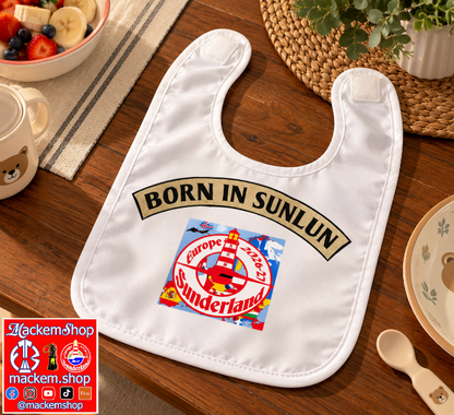 A white baby bib laid flat on a wooden table, printed with a gold 'BORN IN SUNLUN' banner and a colorful 'Europe 2026-27 Sunderland' crest graphic. A mug, plate, spoon, and woven placemat are visible around it, and a 'Mackemshop' logo appears in the lower-left corner.
