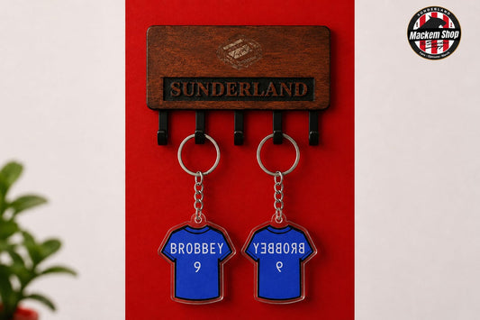 A wooden Sunderland wall hook set with two blue football shirt keychains hanging from black hooks. The keychains are personalized with the name 'BROBBEY' and number 9.
