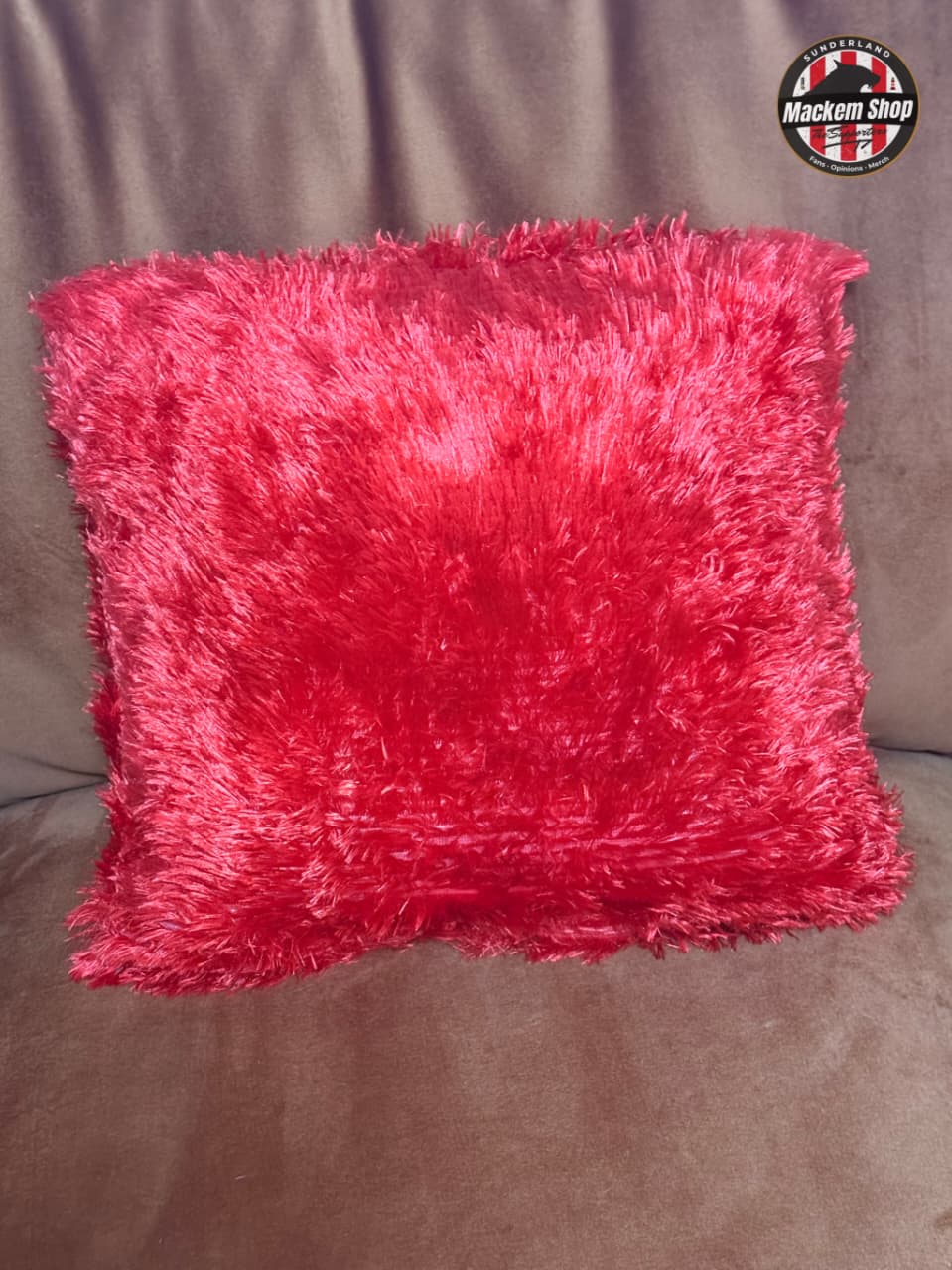 Pink fluffy pillow on a brown couch with a logo in the corner.