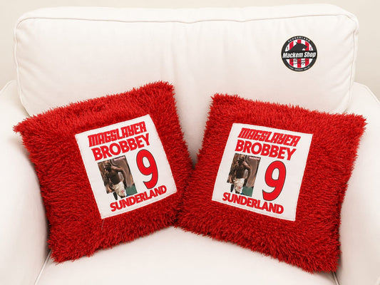 Two red pillows with Brian Brobbey printed text and his shirtless celebration images on a white couch.