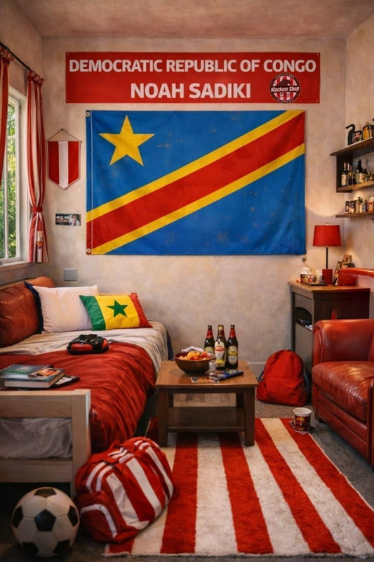 A bedroom scene featuring a large Democratic Republic of Congo flag hanging on the wall, with a red banner above reading 'DEMOCRATIC REPUBLIC OF CONGO NOAH SADIKI'. The room includes a bed with red bedding, a striped rug, a leather chair, and soccer-themed decor.