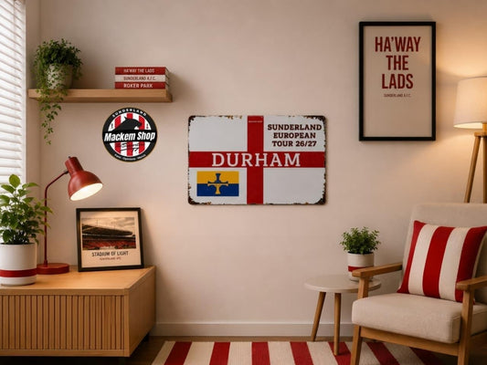 A styled interior room showing a framed Sunderland football-themed wall sign with the word DURHAM and a match graphic, alongside other decor including a striped chair, lamp, shelf, and framed poster.