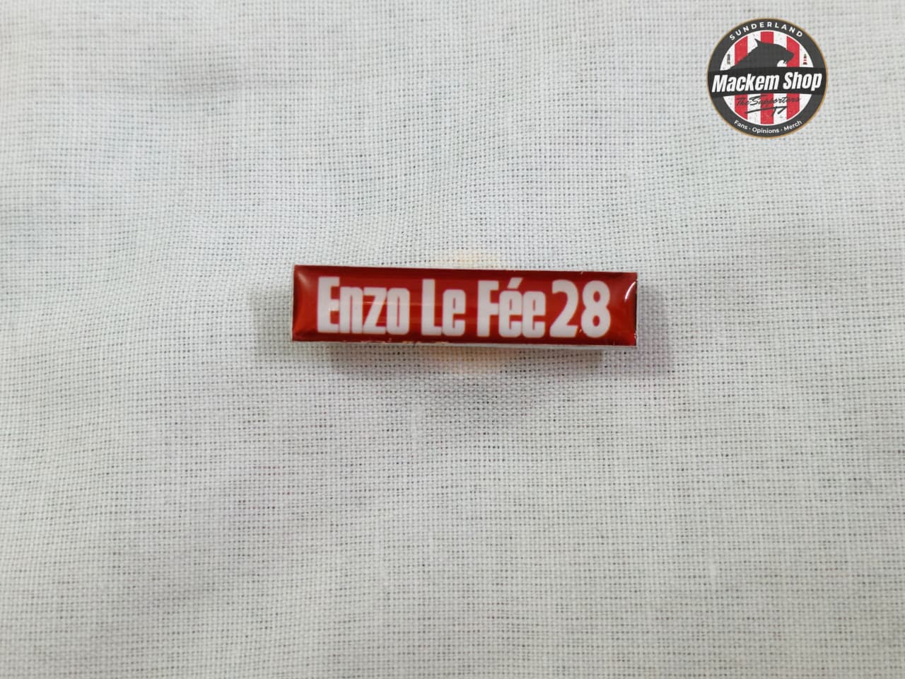 Red and white pin Badge with 'Enzo Le Fèe 28' text on a gray background.
