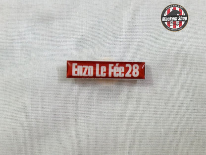 Red and white pin Badge with 'Enzo Le Fèe 28' text on a gray background.