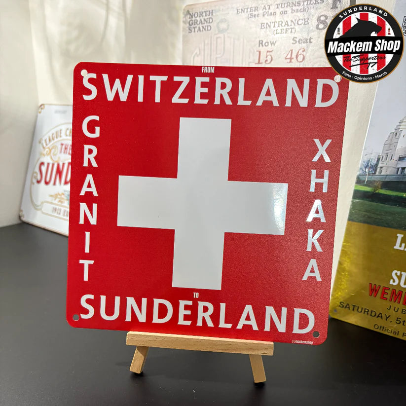 Red sign with white cross and text on a stand, with blurred background