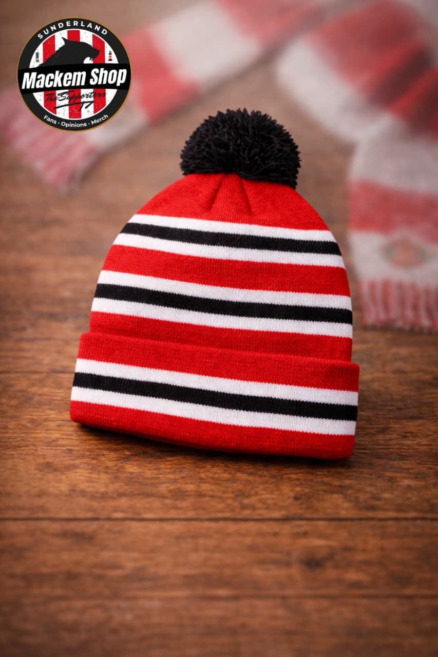 Red and black striped beanie with a pom-pom on a wooden surface, featuring the 'Mackem Shop' logo.