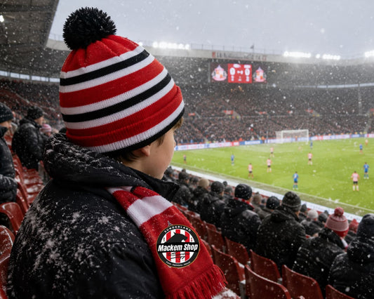 Person wearing a red and black striped beanie and scarf at a snowy soccer stadium.