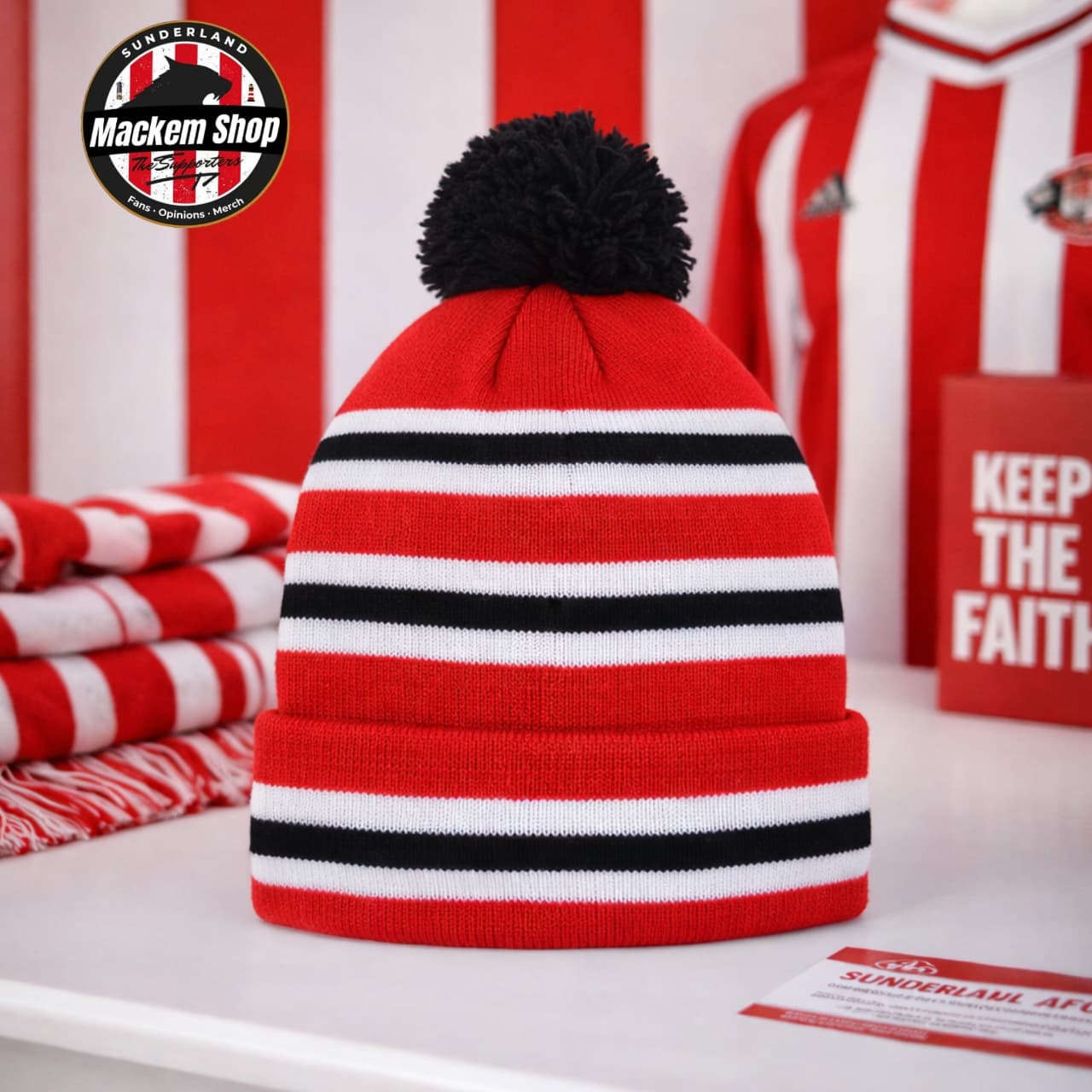 Red beanie with black and white stripes and a black pom-pom on a red and white striped background.