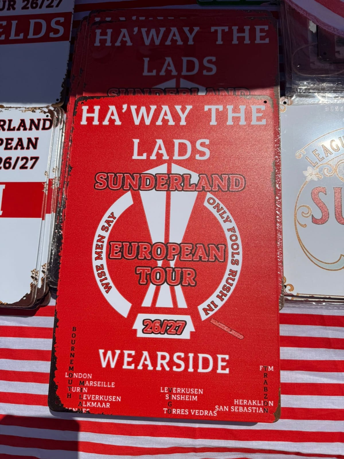Red sign with 'Ha'Way The Lads' text and branding on a striped background