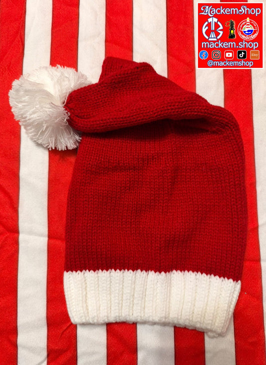 A red and white knitted Santa hat with a fluffy white pom-pom, laid flat on a red and white striped fabric background. A 'MackemShop' logo overlay is visible in the top right corner.