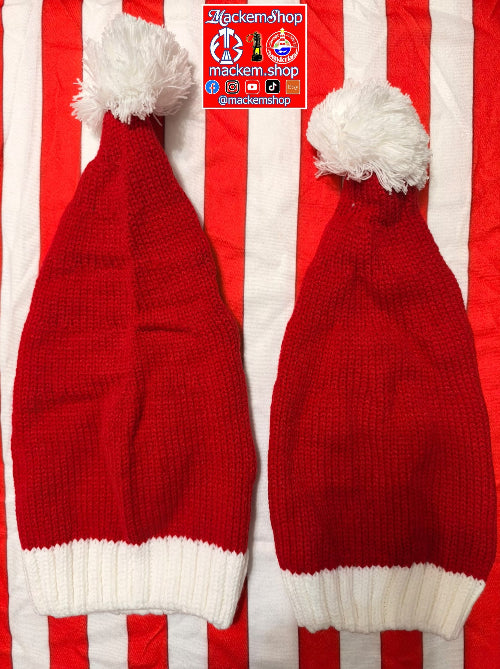 Two red knit Santa hats with white pom-poms and white ribbed cuffs, laid flat on a red and white striped background. A 'MackemShop' logo sticker is visible near the top center.