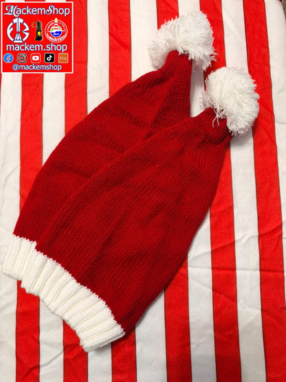 A red knit Santa hat with white pom-poms and a white ribbed cuff, laid diagonally on a red and white striped fabric background. A 'MackemShop' logo overlay is visible in the top-left corner.