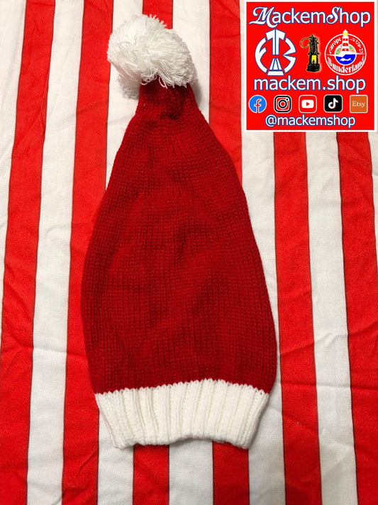 A red knit Santa hat with a white pom-pom and white ribbed cuff, laid flat on a red and white striped fabric background. A red and blue 'MackemShop' logo overlay is visible in the top right corner.