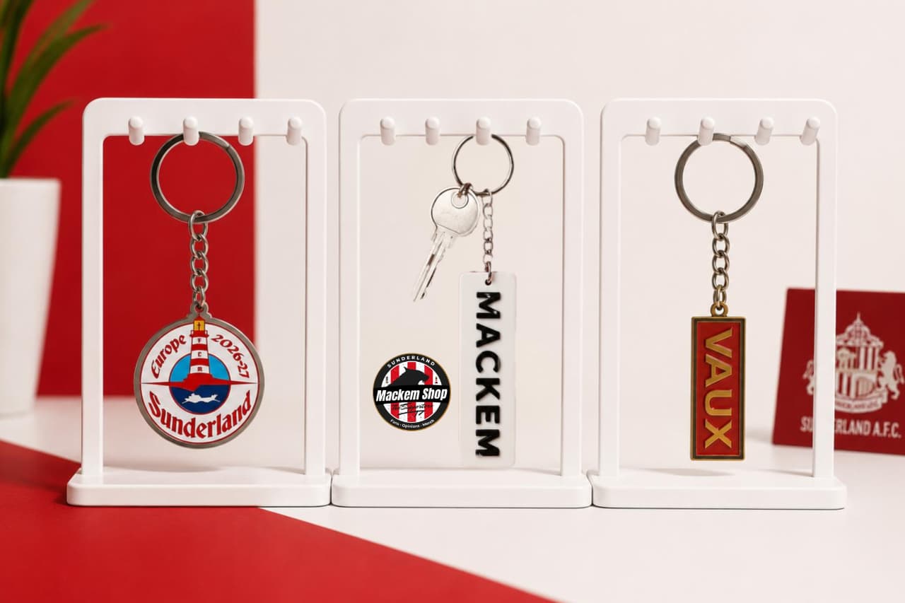 Three white display stands holding Sunderland football-themed keychains on a red and white surface. The keychains include a round lighthouse emblem, a rectangular nameplate reading MACKEM, and Vaux.