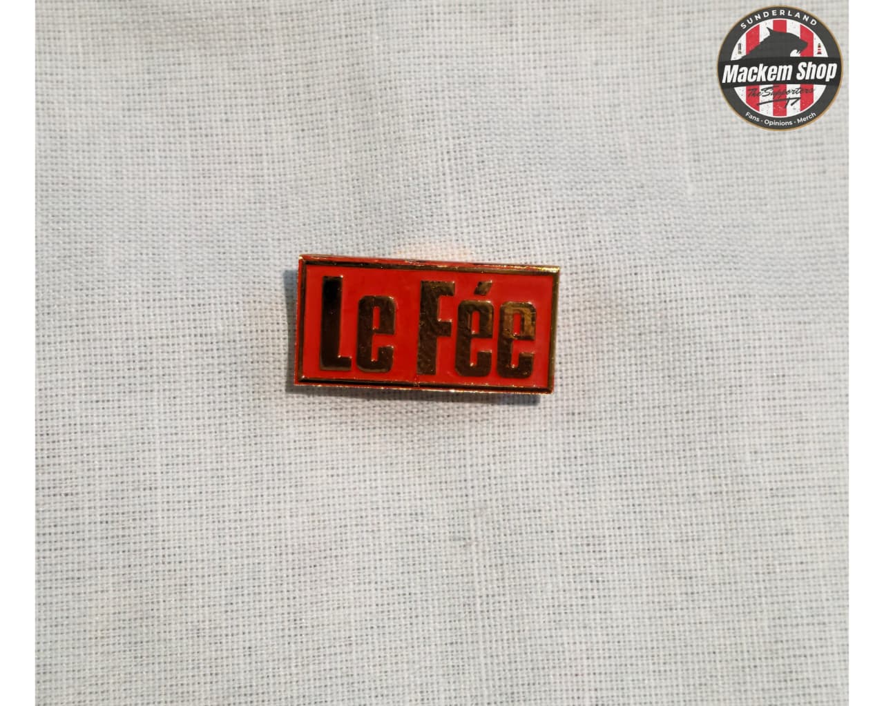 Red and Yellow 'Le Fée' Badge on a textured gray background