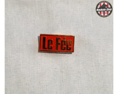 Red and Yellow 'Le Fée' Badge on a textured gray background