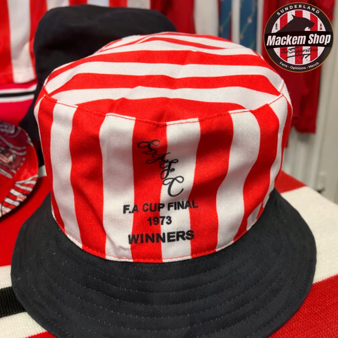 Red and white striped bucket hat with black brim, featuring text 'FA Cup Final 1973 Winners', on a red and white striped background.