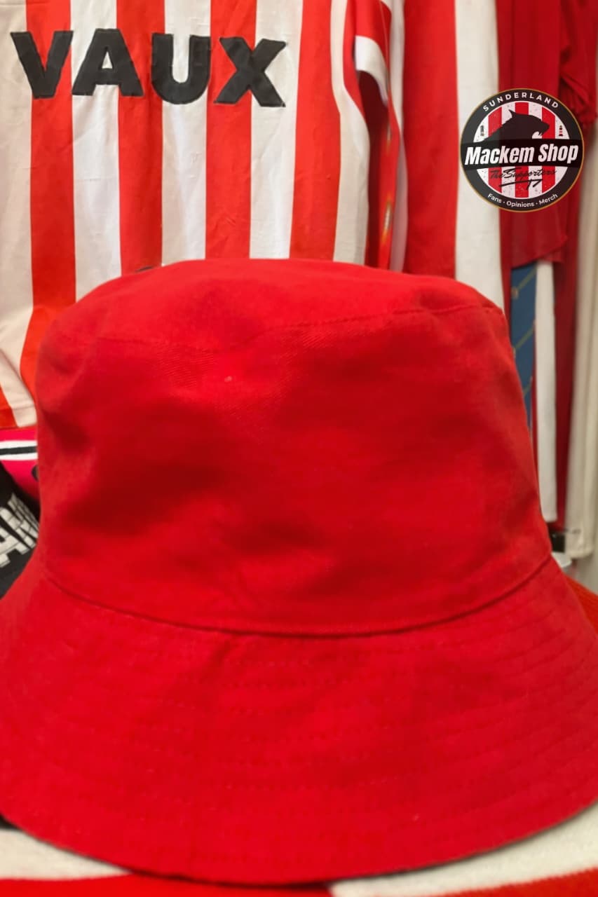 Red bucket hat on a background with striped shirt and 'VAUX' branding.