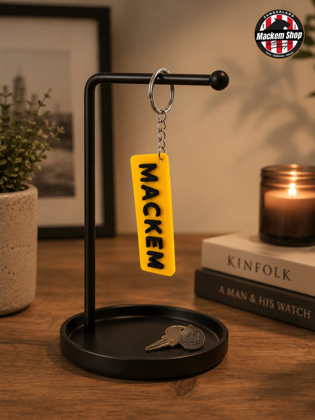 Yellow keychain with 'MACKEM' on a black stand with a candle and books in the background.