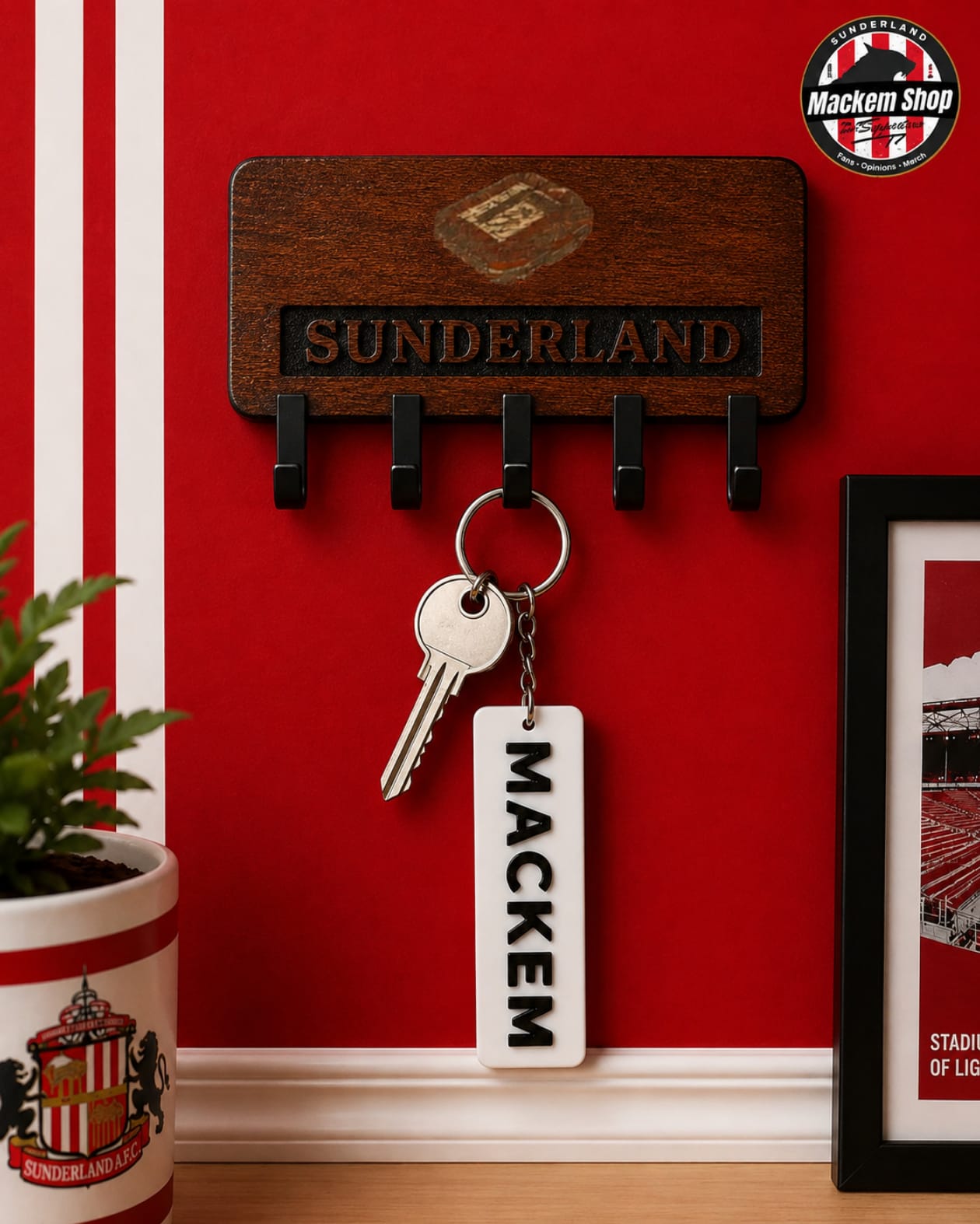A wooden Sunderland key holder mounted on a red wall, holding a keyring with a white rectangular keychain that reads MACKEM. A Sunderland football club crest is visible on the pot and framed print, and a MackemShop logo appears in the top right corner.