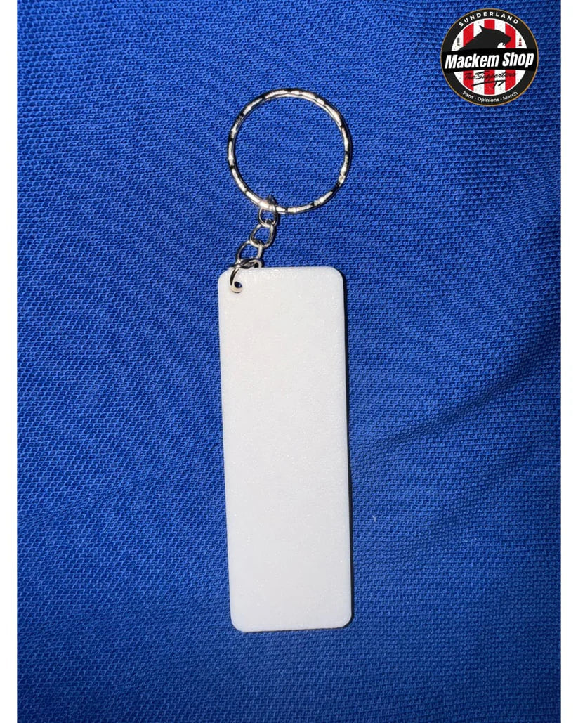 A blank white rectangular acrylic keychain tag with a silver split ring and chain, displayed on a textured blue background. A 'Mackem Shop' logo is visible in the top right corner.