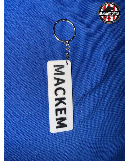 A white rectangular acrylic keychain with the name 'MACKEM' printed vertically in black, attached to a silver metal key ring, displayed on a textured blue fabric background. A circular 'Mackem Shop' logo is visible in the top right corner.