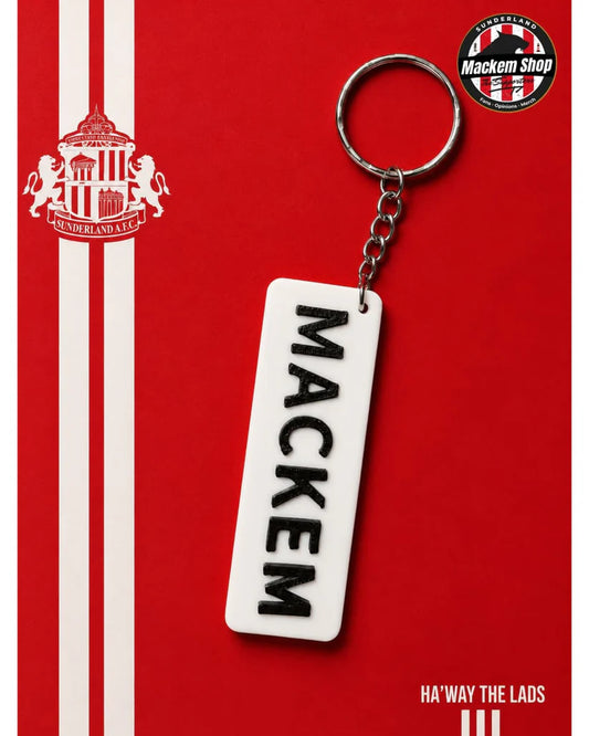 A Sunderland AFC themed keychain featuring a white rectangular tag with the name 'MACKEM' printed vertically in black, attached to a silver metal split ring. The background is a vibrant red with white stripes, the Sunderland AFC club crest on the left, and a circular 'Mackem Shop' logo in the top right corner.