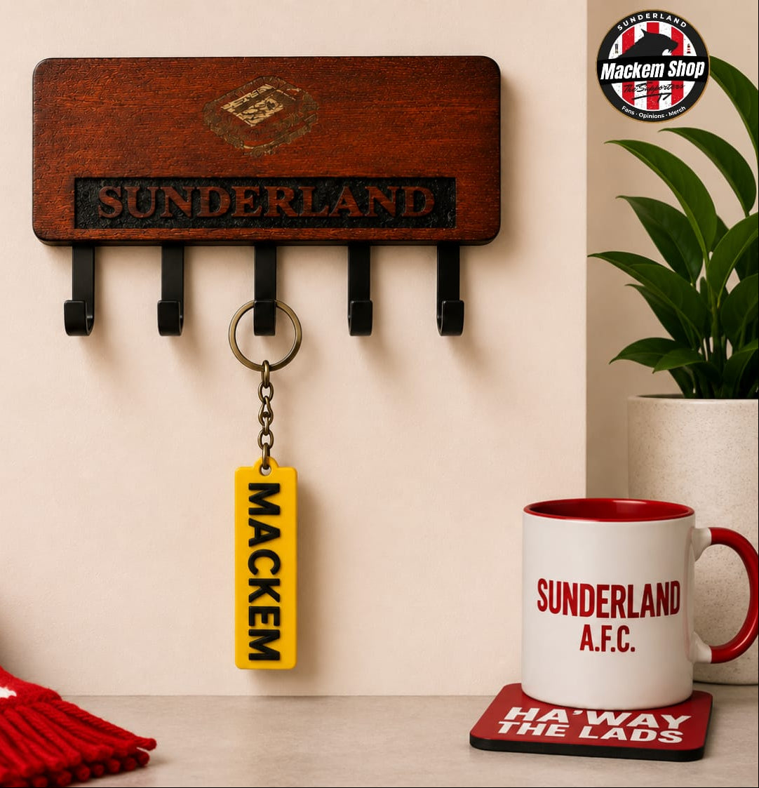 A wooden Sunderland AFC wall hook rack with five black hooks, shown in a styled home environment with a yellow 'MACKEM' keychain hanging from one hook, a red and white striped scarf, a white mug, and a plant.