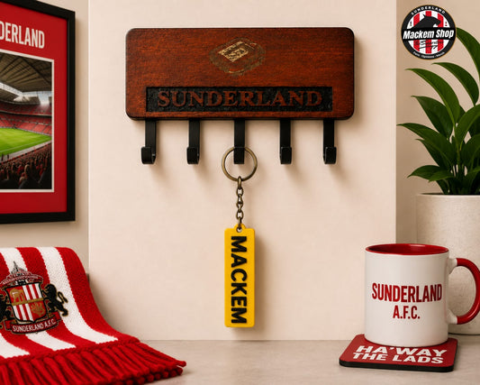 A wooden Sunderland AFC wall hook rack with five black hooks, shown in a styled home environment with a yellow 'MACKEM' keychain hanging from one hook, a red and white striped scarf, a white mug, and a plant.