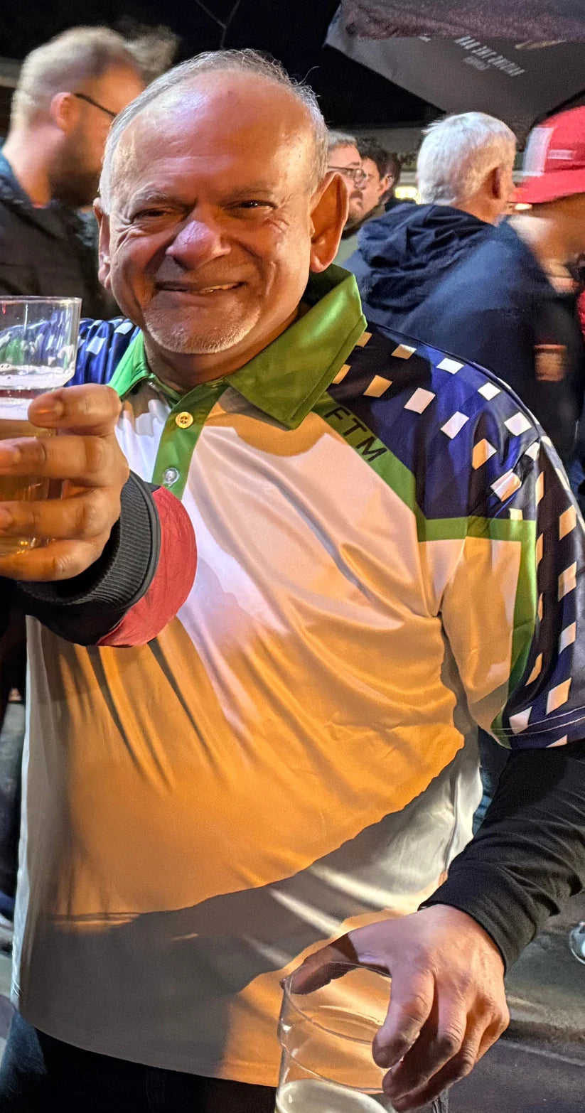 Man in Golf polo shirt by Mackem shop holding a glass, surrounded by people at an outdoor event
