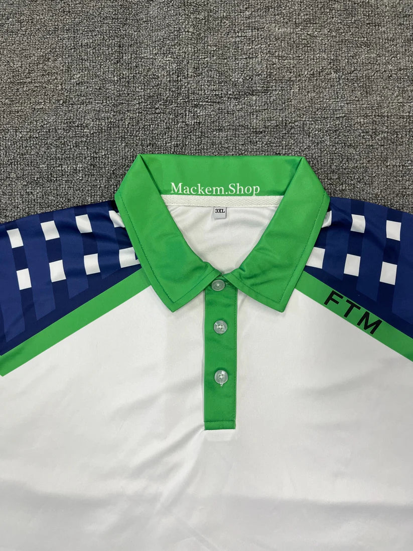 White polo shirt with green collar and blue sleeves featuring 'Mackem Shop' branding on a gray background.