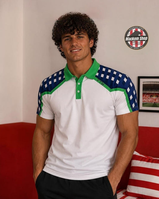 A man wearing a white short-sleeve polo shirt with green and navy blue checkered shoulder panels, standing in front of a red couch and a white wall with a circular 'Mackem Shop' logo.